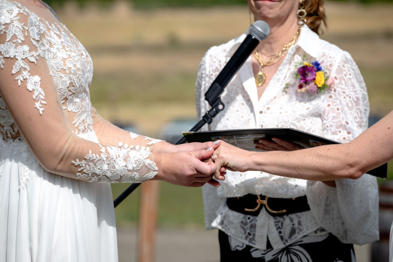 Brides exchange wedding rings at wedding ceremony outside.