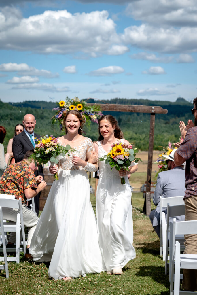 brides walking back down the isle after getting married with thier wedding bouquets. the flowers have lots of sunflowers and bright colors in them.